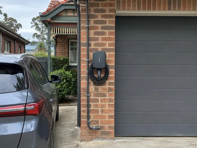 Wall-mounted EV charger on a brick garage wall beside a driveway in Chatswood