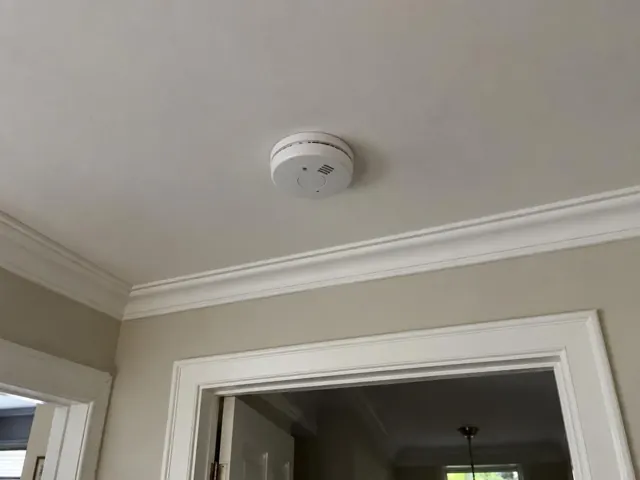 Ceiling-mounted smoke alarm on a plaster ceiling above a doorway in a residential home in Lindfield